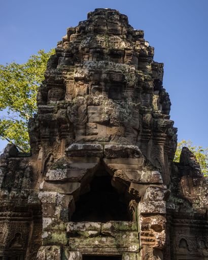 Ancient stone temple ruins under a clear blue sky, showcasing intricate carvings and historical architecture, surrounded by lush greenery.