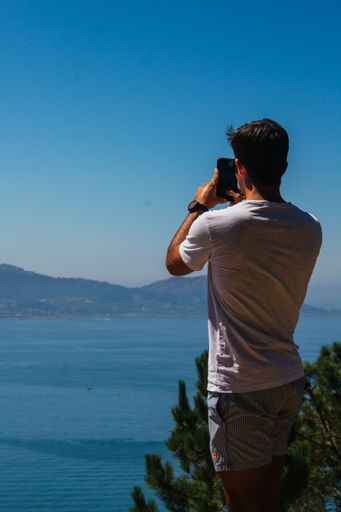 A vertical shot of a young Spanish Caucasian man taking a photo of the beautiful view, with his phone
