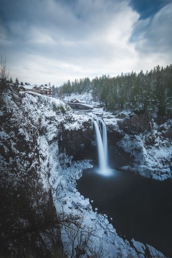 A beautiful vertical shot of waterfalls on glacier mountain near trees in Winter