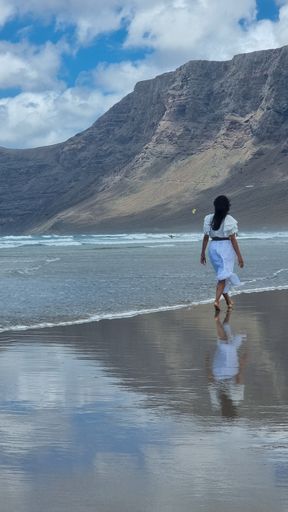 A vertical shot of a Caucasian woman walking on the beach with a beautiful white dress in Spain
