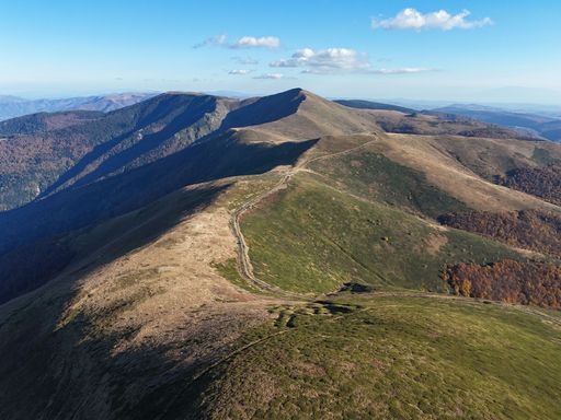 Aerial view of a scenic mountain range with lush greenery and a clear blue sky, showcasing nature's beauty.