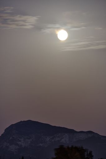 A vertical shot of a shining sun in a dark sky over a mountain