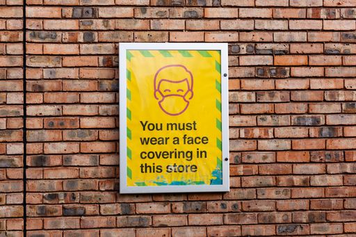 A large sign is mounted on a brick wall stating that a face covering must be worn while in the store. Covid, face mask, new normal concept