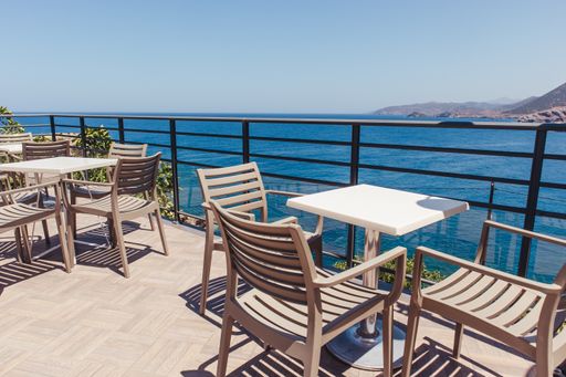 Empty plastic chairs and tables at an outdoor cafe on a balcony with a view of the sea