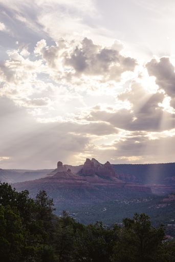 A breathtaking view of the Sedona red rocks under a dramatic cloudy sky with sun rays piercing through