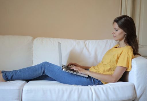 An adult brunette woman lying on the sofa and working on her laptop at home