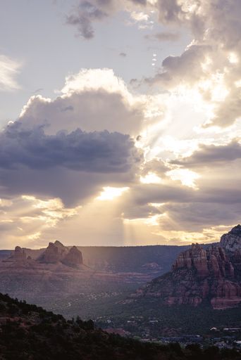 A scenic view of Sedona's red rock formations under dramatic clouds with sun rays piercing through