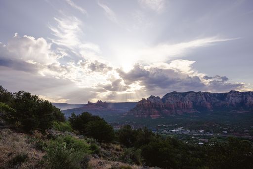 A stunning view of Sedona's red rock formations under a dramatic sky with sun rays breaking through clouds, showcasing nature's beauty.