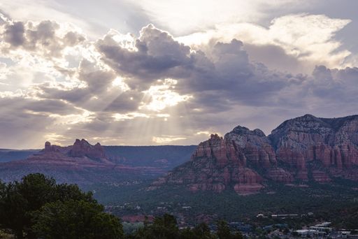 Scenic view of Sedona's red rock formations under dramatic clouds and sunbeams, capturing the natural beauty of Arizona's landscape.