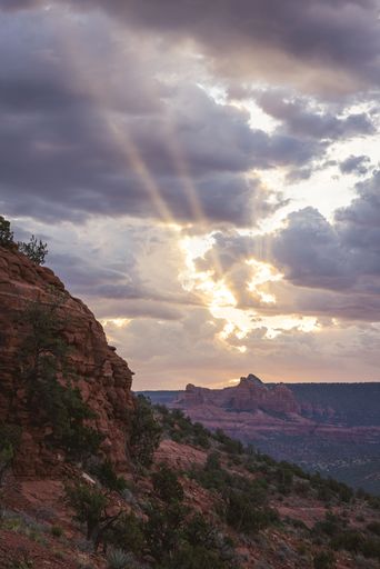Sun rays breaking through clouds over a red rock landscape in Sedona, Arizona, showcasing the dramatic beauty of the American Southwest.