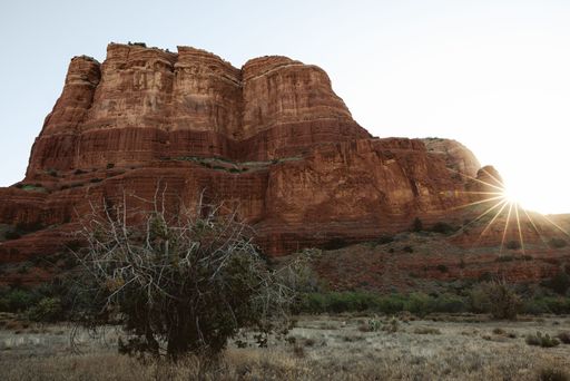Scenic view of Sedona's red rock formations with sunflare at sunset, capturing the rugged landscape and natural beauty.