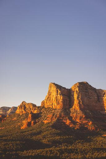 A stunning view of Sedona's red rock formations under a clear blue sky at sunset, capturing the vibrant colors of the landscape.