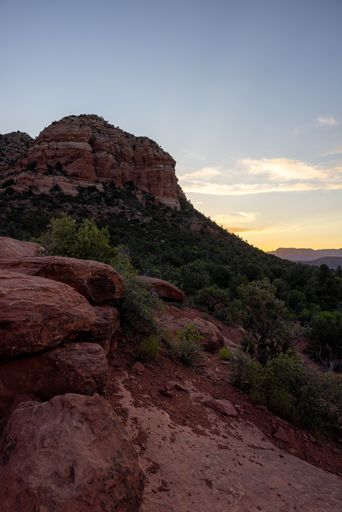 A scenic view of Sedona's red rock formations at sunset, with a clear sky and lush greenery.