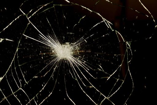 A close-up of shattered glass. A network of cracks radiates outward from a central point of impact.