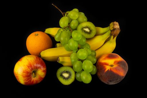 A closeup shot of sliced kiwi, bananas, peaches, grapes, and orange isolated on a dark background