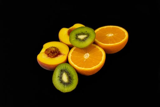 A closeup shot of fresh sliced orange, peach, and kiwi isolated on a dark background