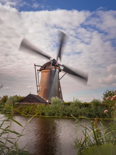A working windmill on the coast of the river against a cloudy sky in Kinderdijk