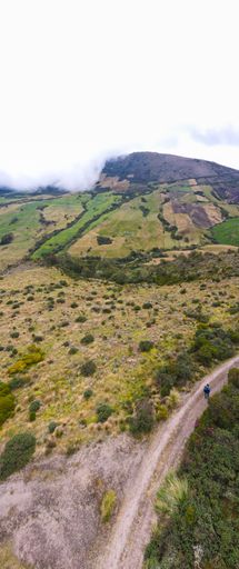 A vertical shot of a road surrounded by green lands and misty mountains