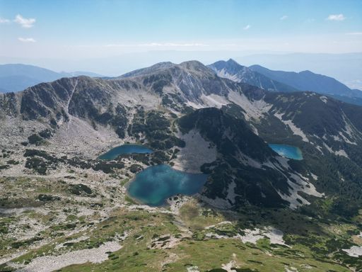 Aerial view of the Pirin Mountains with clear blue lakes and rugged terrain under a bright sky in Bulgaria.