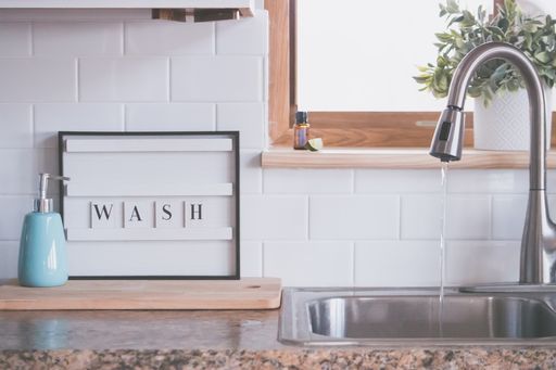 A closeup shot of a "Wash" sign, soap dispenser and a sink raising awareness of the existing pandemic, on a white tile background