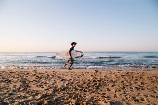 A young black surfer with afro hair running with surfboard along the sea shore