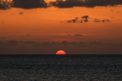 A glorious scenery of the sun setting down on the horizon by the ocean with orange ombre sky