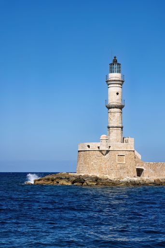 A historic lighthouse standing on a rocky coastline under a clear blue sky in Chania, Crete.