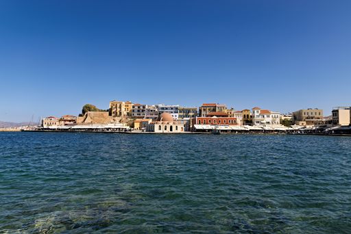 A scenic view of Chania's old harbor with historic buildings against a clear blue sky, Crete, Greece.