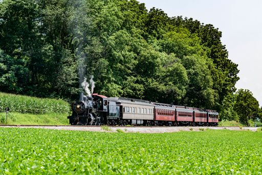 A restored steam passenger train blowing smoke and steam on a sunny summer day