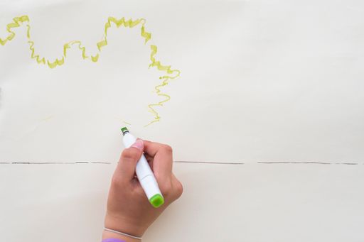 A woman's hand draws a sketch of the future drawing with a green marker on the white surface of the paper.