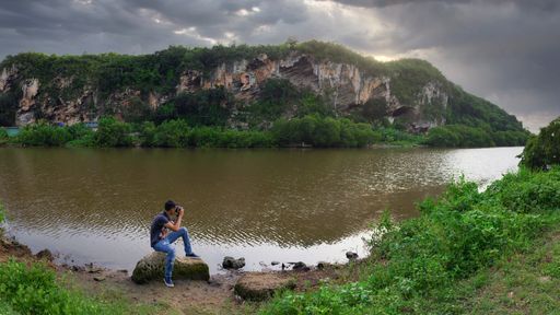 A Hispanic man sitting on a rock near a calm lake during sunrise in Yurumi Valley at Matanzas, Cuba