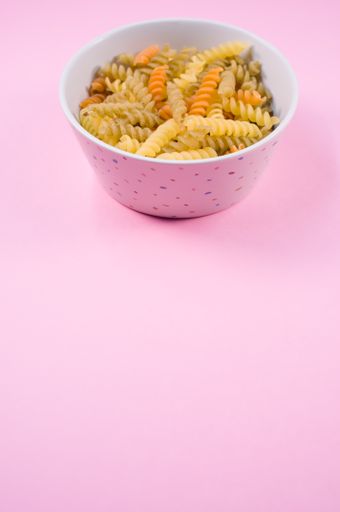 Little white pottery with colored fusilli pasta isolated on a pink background with text space