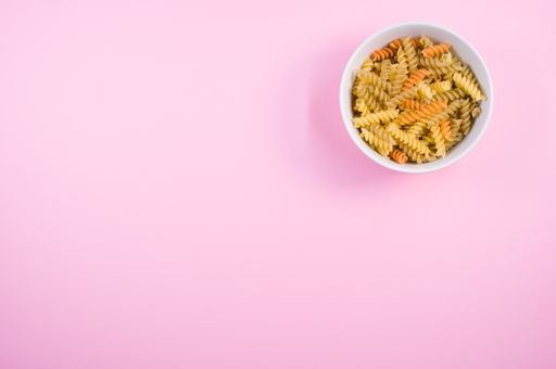 Little white pottery with colored fusilli pasta isolated on a pink background with text space