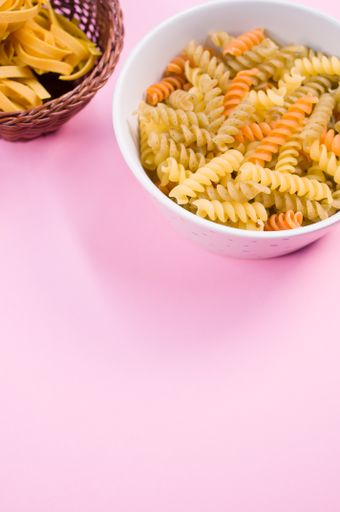 Little white pottery with colored fusilli pasta isolated on a pink background with text space
