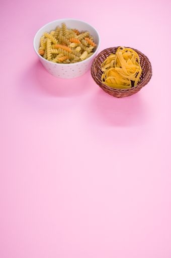 Little white pottery with colored fusilli pasta isolated on a pink background with text space