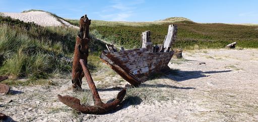 An eerie scenery of an old damaged wooden boat with a rusty anchor on a sandy beach