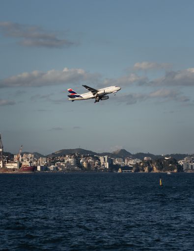 An airplane flying over a blue sea on the background of buildings and the sky