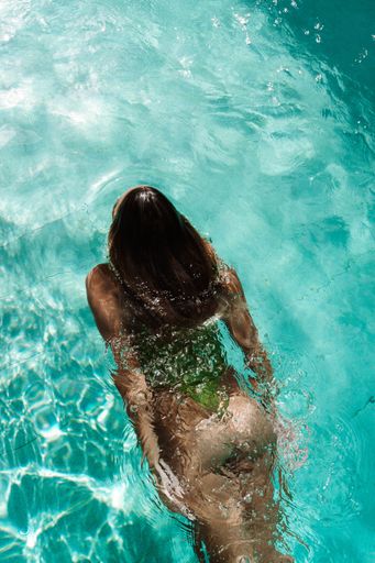 A woman swimming in a clear turquoise pool, sunlight reflecting on the water surface, creating a serene and refreshing atmosphere.