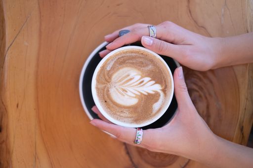 A top view of a woman's hands softly holding a mug of cappuccino in the morning on a woody table