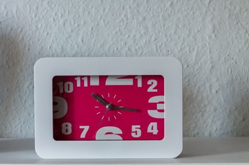 A closeup of a white square alarm clock on the nightstand in the bedroom