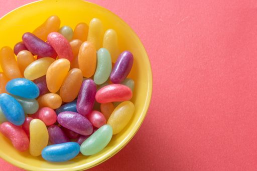 A top view of colorful jelly beans in a bowl, on a red surface