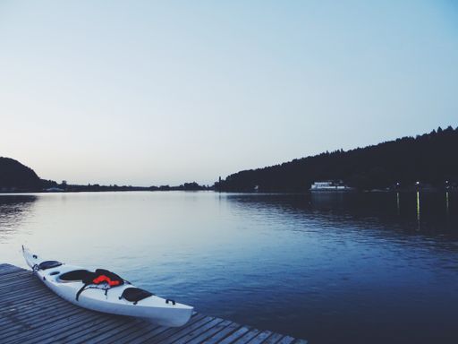 A beautiful shot of a lake with a white kayak on a brown wooden dock
