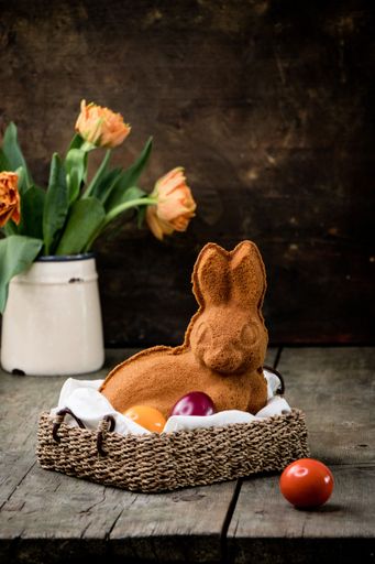 An easter bunny cookie in a wicker basket with colorful eggs and tulips in a rustic setting.