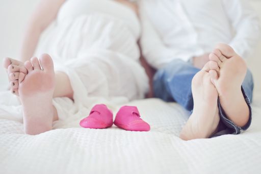 A concept of a family and pregnancy- a couple laying on a bad and small pink baby shoes between their foot