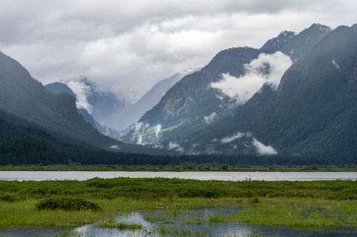 A beautiful scene of high green dirty mountains under gray cloudy sky over green fields and river eater