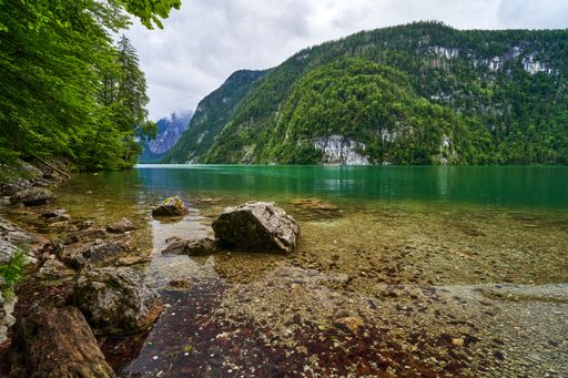 A serene view of a clear lake surrounded by lush green mountains under a cloudy sky, perfect for nature enthusiasts.