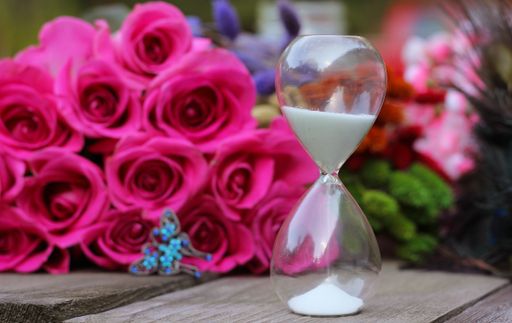 A selective shot of hourglass, pink roses, and butterfly jewelry on a wooden table
