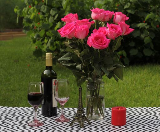 A bouquet of pink roses on an outdoor table with wine and candle - romantic setup