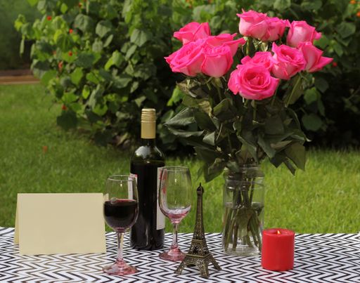 A view of a bouquet of roses with a bottle of wine, two glasses, candle, statuette, and postcard on the ground