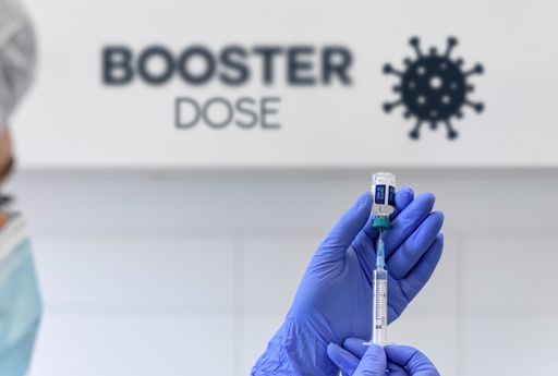 Hand in gloves holding syringe and vaccine for covid-19. Booster dose text and corona virus icon.